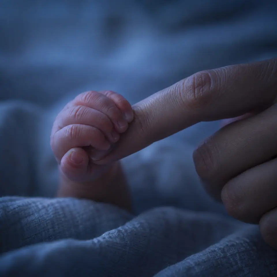 Mano de un bebé que sostiene un dedo, en luz azul